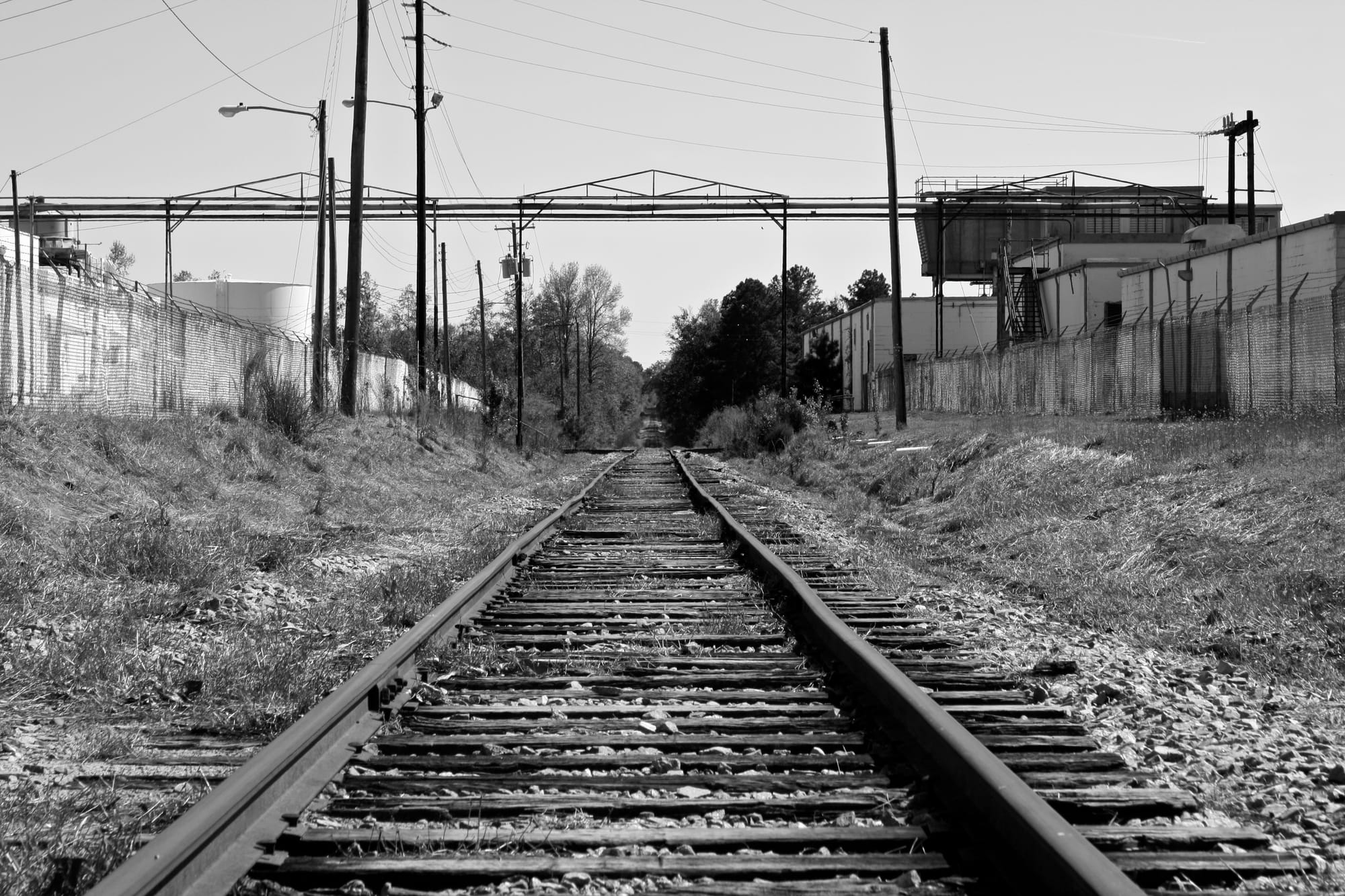 Black and white photo of an empty railroad track with old industrial buildings on either side